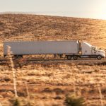 a white semi truck driving down a rural road